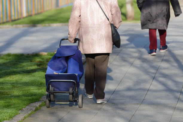 starsza kobieta z torbą na kółkach na ulicy, widok z tyłu - women walking shopping street zdjęcia i obrazy z banku zdjęć