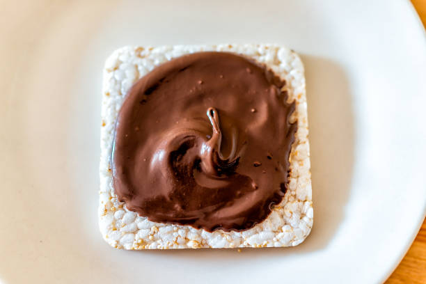 チョコレートヘーゼルナッツとライスケーキのフラットトップクローズアップ茶色のソースまたはシロップで広がるヴィーガンベジタリアンスナックデザート1枚白プレート上 - short paste ストックフォトと画像