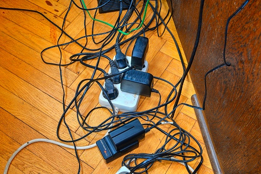 Tangled wires and battery charges on parquete floor. Domestic appliances.  Wires mess in domestic room.