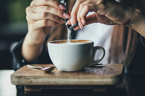 La mano de la muchacha vierte azúcar en su café. De cerca photo
