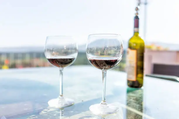 Terrace patio in Italy with bottle and two glasses of red wine on glass table with bokeh background of mountains