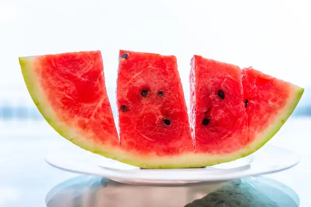 Summer day with vivid vibrant colorful red watermelon slice cut outside in Italy on white plate and glass table with seeded black seeds