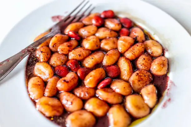 Closeup of fresh red wine sauce potato gluten free wheat gnocchi on white plate with lupine beans in Italian Italy restaurant with fork and olive oil