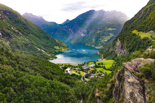 Majestic view on the Geirangerfjord with mountains, forests, and a settlement in Norway Majestic view on the Geirangerfjord with mountains, forests, and a settlement is captured on a summer day. In the valley, there is a body of water surrounded by majestic rocky mountains. In the valley, there is also a settlement just on the shore of the fjord. geirangerfjord stock pictures, royalty-free photos & images