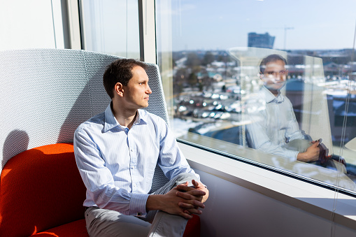 New modern office room in building with red chair closeup by glass window with business man sitting looking at corporate view through