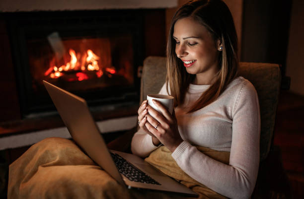 femme utilisant l'ordinateur portatif près de la cheminée - blanket fireplace winter women photos et images de collection