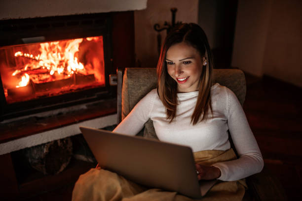 femme utilisant l'ordinateur portatif près de la cheminée - blanket fireplace winter women photos et images de collection