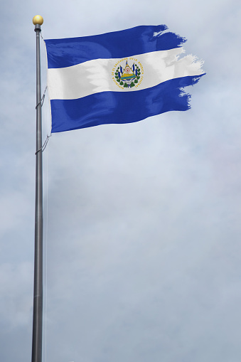 Worn and tattered El Salvador flag blowing in the wind on a cloudy day
