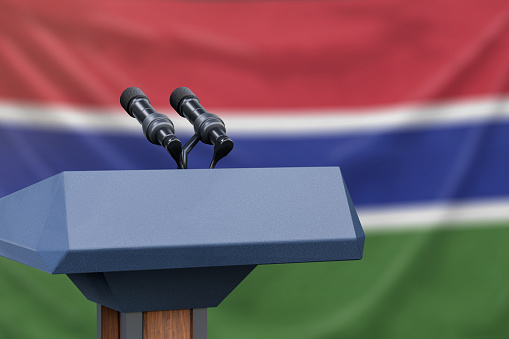 Podium lectern with two microphones and Gambia flag in background