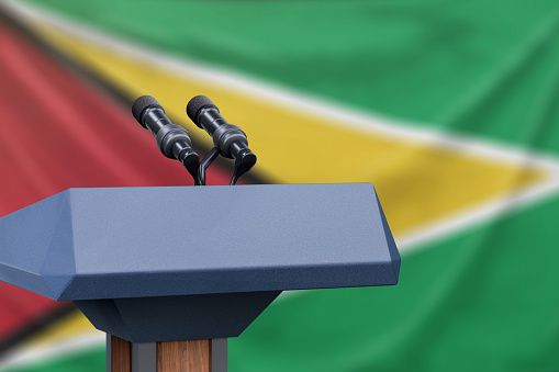 Podium lectern with two microphones and Guyana flag in background