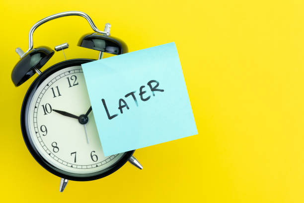 Sticky post with handwriting the word Later stick on alarm clock on solid yellow background with copy space using as procrastination, self discipline or laziness concept stock photo