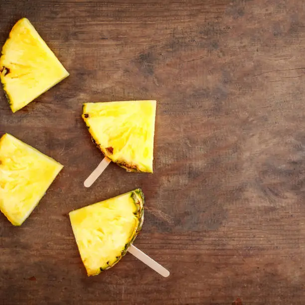 Photo of Pineapple  slice popsicles on a brown rustic wood background. Flat lay. Tropical Summer concept 