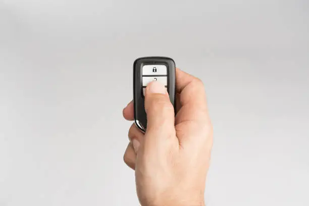 Photo of Hand of man holding and push remote control of car to lock unlock or start isolated on gray background