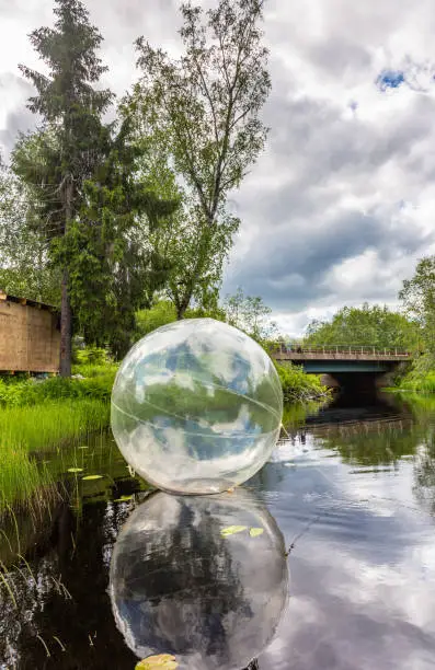 Photo of An inflatable transparent ball floats on the surface of a reservoir on the Ruskeala Waterfalls in a forest under a blue sky with clouds, Karelia. Russia