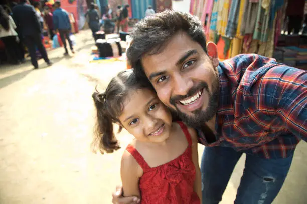 Happy Indian father taking selfie with daughter at street market