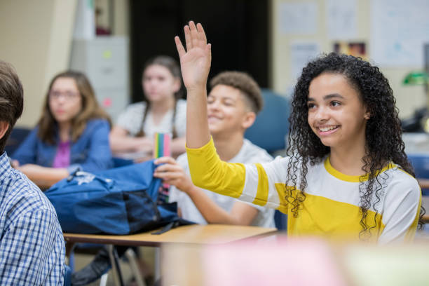 Cute high school girl raising hand to answer question in classroom Cute high school girl raising hand to answer question in classroom teenage high school girl raising hand during class stock pictures, royalty-free photos & images