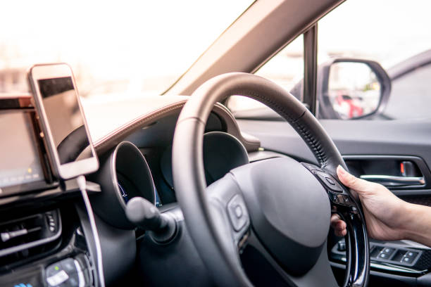 istock Male driver hand holding on steering wheel using smartphone for GPS navigation. Mobile phone mounting with magnet on the car console in modern car. Urban driving lifestyle with mobile app technology 1135678310