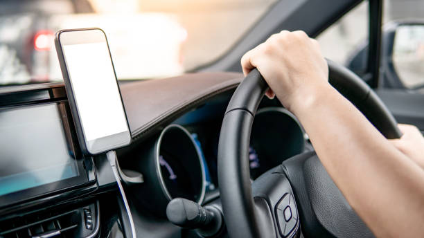 gps ナビゲーションのためのスマートフォンを使用してステアリングホイール上の男性ドライバーハンドホールディング。近代的な車の中で車のコンソール上の磁石と携帯電話のマウント。モ - car map car rental land vehicle ストックフォトと画像