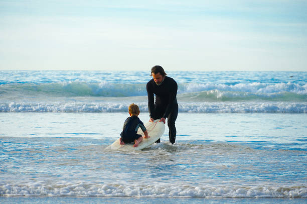 padre o instructor enseñando a niño pequeño cómo surfear en el mar. - surfing beach family father fotografías e imágenes de stock