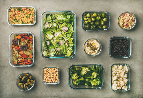 Various healthy vegan or vegetarian dishes in glass containers. Flat-lay of fresh and cooked vegetable salads, legumes, beans, fermented olives, sprouts, humus dip and couscous for making vegan take-away lunch or Buddha bowl, top view. Spring menu, clean eating or dieting food concept