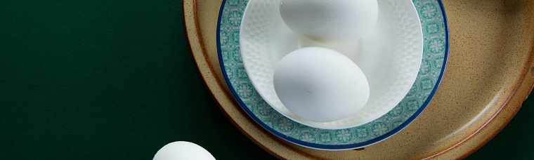 A single egg in a white tempered glass eggcup and Chinese porcelain saucer ready for eating. It is placed on a Chinese Rosewood dining table. No people.