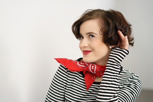 Cute sexy young woman in a stylish scarf and makeup holding her hand to her ear as she leans towards the camera with a smile