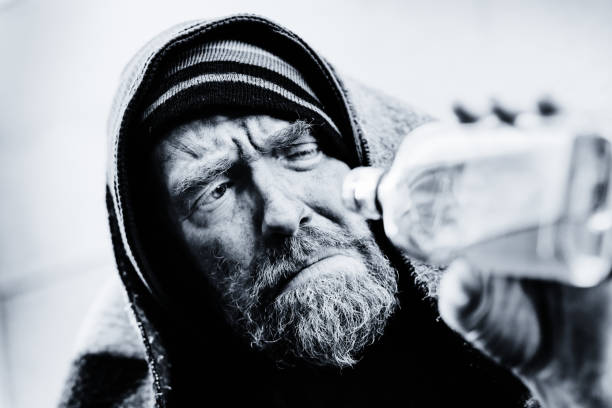 istock Frowning, desperate homeless man holds up half-empty liquor bottle 1135692242