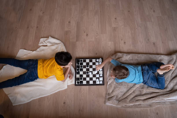 Two boys playing chess laying on the floor and thinking hard stock photo