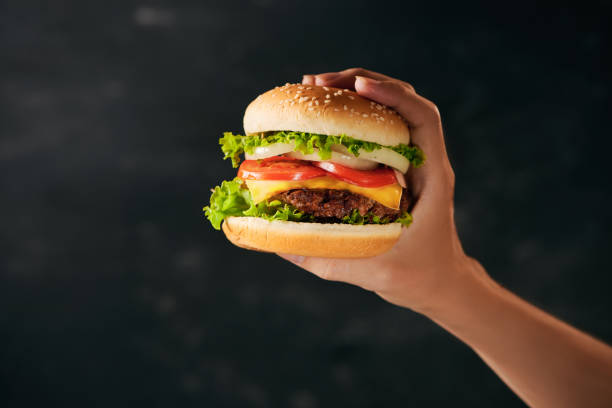 istock Tasty burger sandwich in hand isolated on black background 1135702037