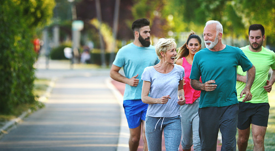 Closeup front view of group of mixed age people having a light jogging at a local park on a sunny summer afternoon. There are two seniors and three mid 20's people.