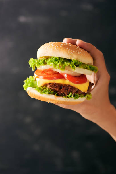 istock Tasty burger sandwich in hand isolated on black background 1135702067