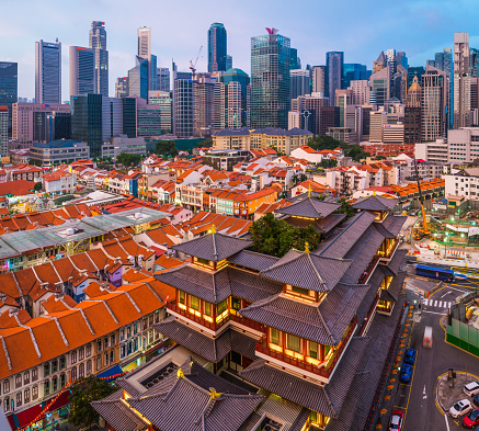 The crowded skyscraper cityscape of the Downtown Core overlooking the warmly illuminated Buddha Tooth Relic Temple in Chinatown, Singapore.