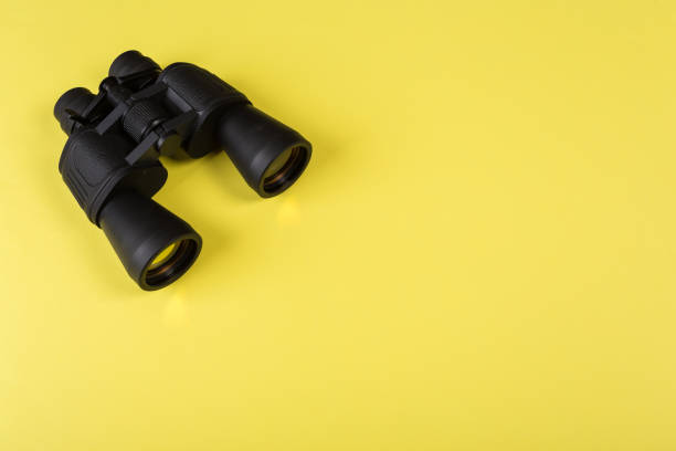 istock Black binoculars with orange lens on yellow background 1135703249