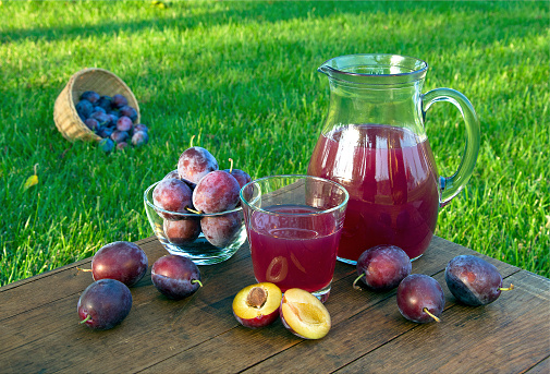 Prune juice in the carafe and glass with plums. Horizontal outdoors shot.