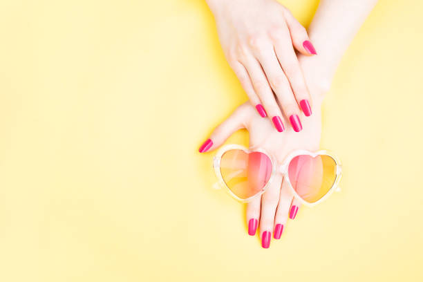 Summer manicure background. Beautiful female hands with perfect vibrant nails on yellow background. Heart shape sunglasses. Hands and nails care concept. Flat-lay, top view. Copy space.