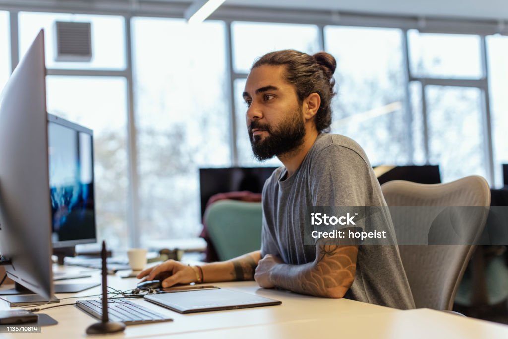 Porträt des stilitischen Hipsters Guy mit Tattoo auf Hand, schreibt Notizen im Computer im Büro - Lizenzfrei Designberuf Stock-Foto