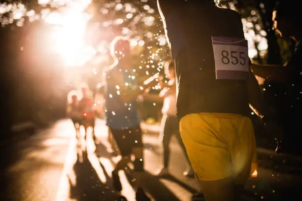 Unrecognizable athlete taking refreshment while running marathon race at sunset.