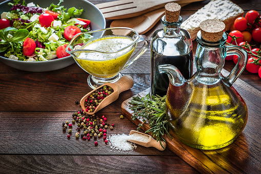 High angle view of some ingredients for dressing a salad like salt, pepper, vinaigrette dressing, fine herbs, tomato, vinegar and olive. A salad without dressing is at the left top corner. Low key DSLR photo taken with Canon EOS 6D Mark II and Canon EF 24-105 mm f/4L