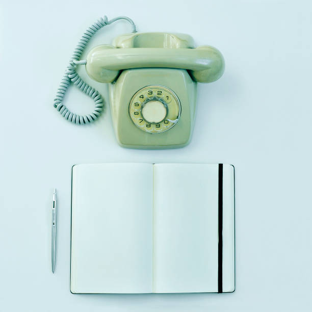 high-angle shot of a rotary telephone, a pen and a blank notepad on a table