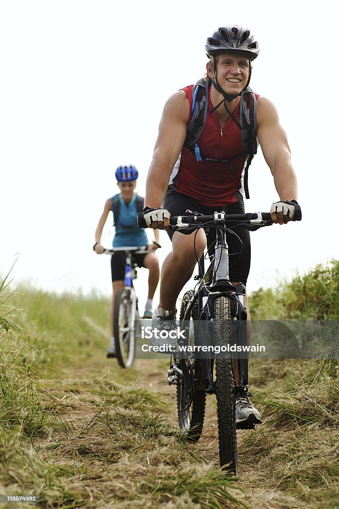 Muscle man and fit woman mountain biking Happy couple riding bicycles outside, healthy lifestyle fun concept Cycling Stock Photo