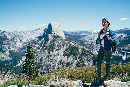 full length of healthy hiker girl standing relaxing sightseeing in nature hike half dome in background. Beautiful young woman hiking happy with cap travel in Yosemite National Park California USA.