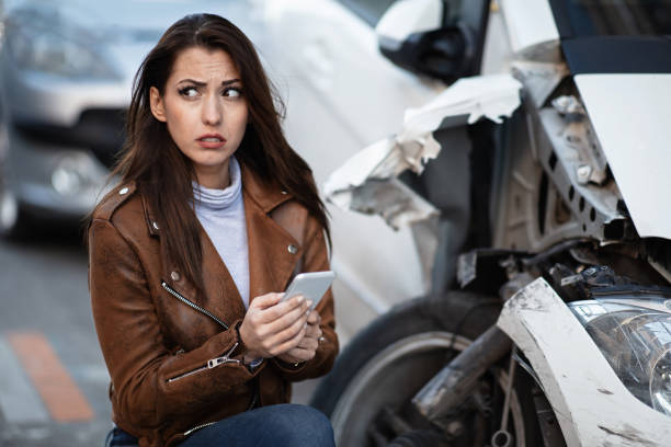 istock Petrified woman using smart phone next to her crashed car. 1135750757