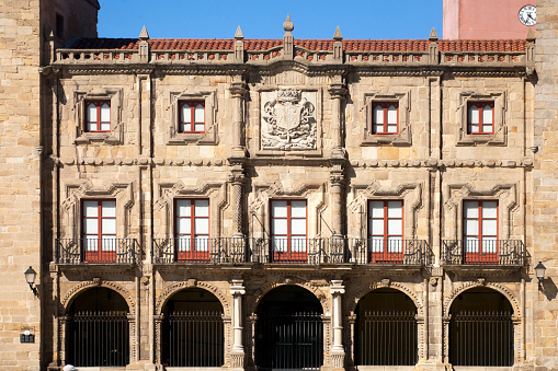 Gijon, Spain-August 31, 2018: Front view of Revillagigedo palace stone facade, Gijon, Asturias, Spain. Ancient monument XVIII century with coat of arms, windows, balconies,arcade, arches, clear blue sky.