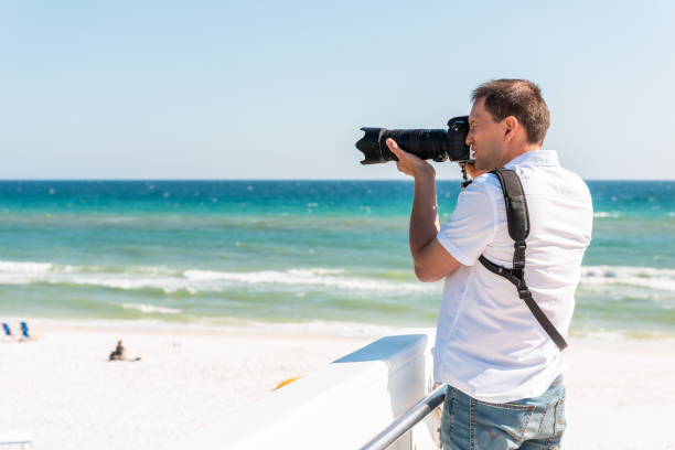 istock Young photographer man taking picture on beach during sunny day in Seaside, Florida panhandle town village with ocean by steps 1135760873