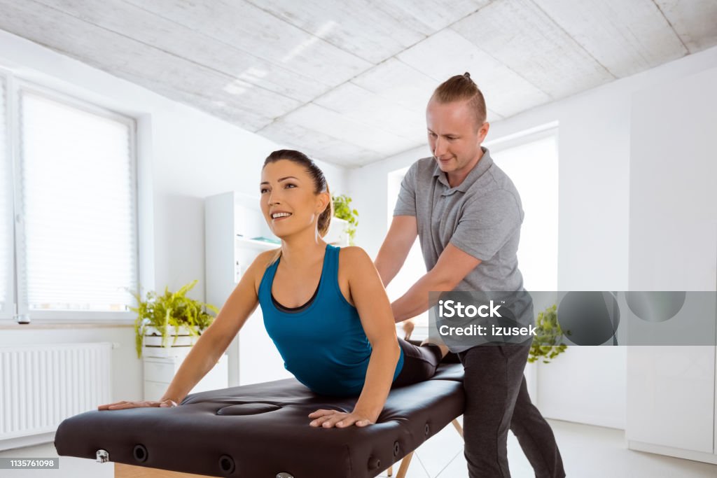 Massage therapist massaging young woman Physiotherapist giving back massage to young woman. Patient lying on massage table. Adult Stock Photo
