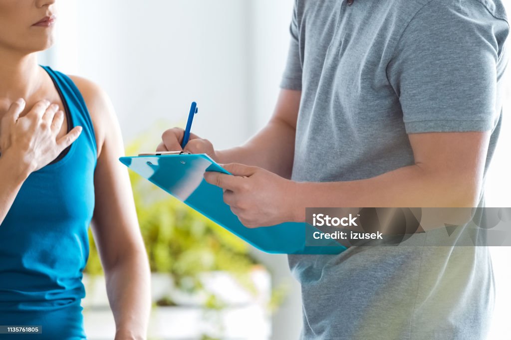 Physical therapist examining young woman in rehabilitation center Young woman talking with male physical therapist in his office, having a medical interview. Occupational Therapy Stock Photo