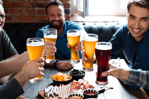 Happy male friends toasting beer glasses while sitting at table. Men enjoying drinks during weekend in restaurant. They are spending leisure time in pub.