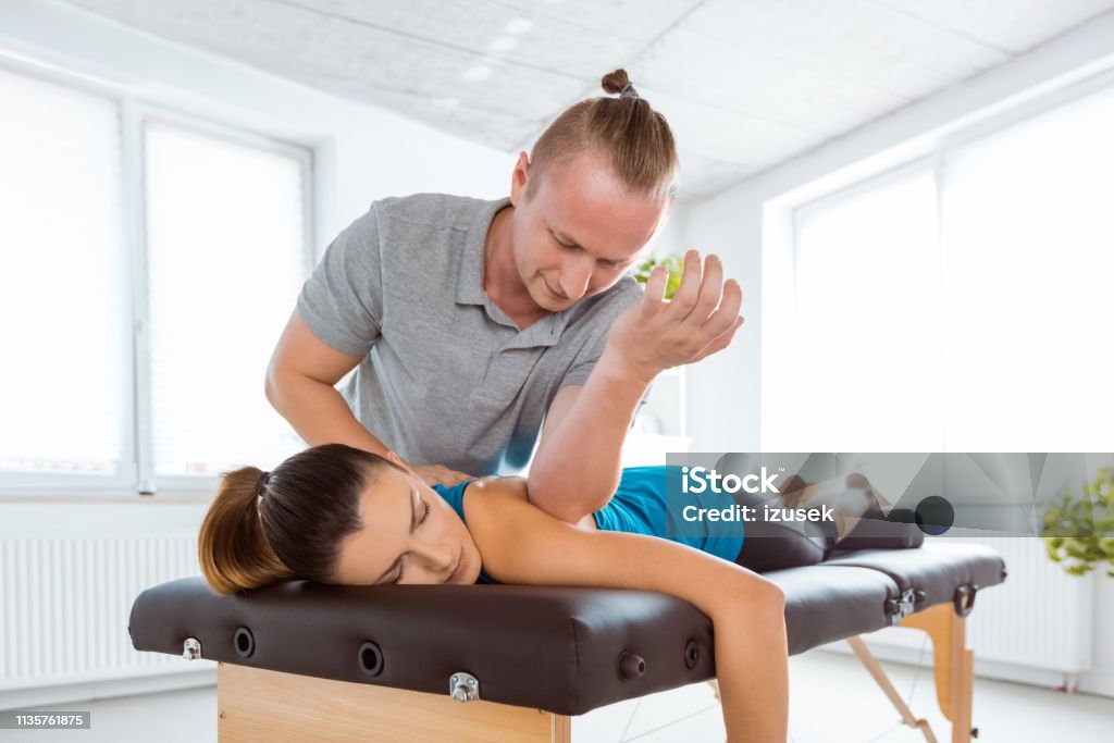 Physiotherapist massaging young woman Manual therapist giving back massage to young woman. Patient lying on massage table. Adult Stock Photo