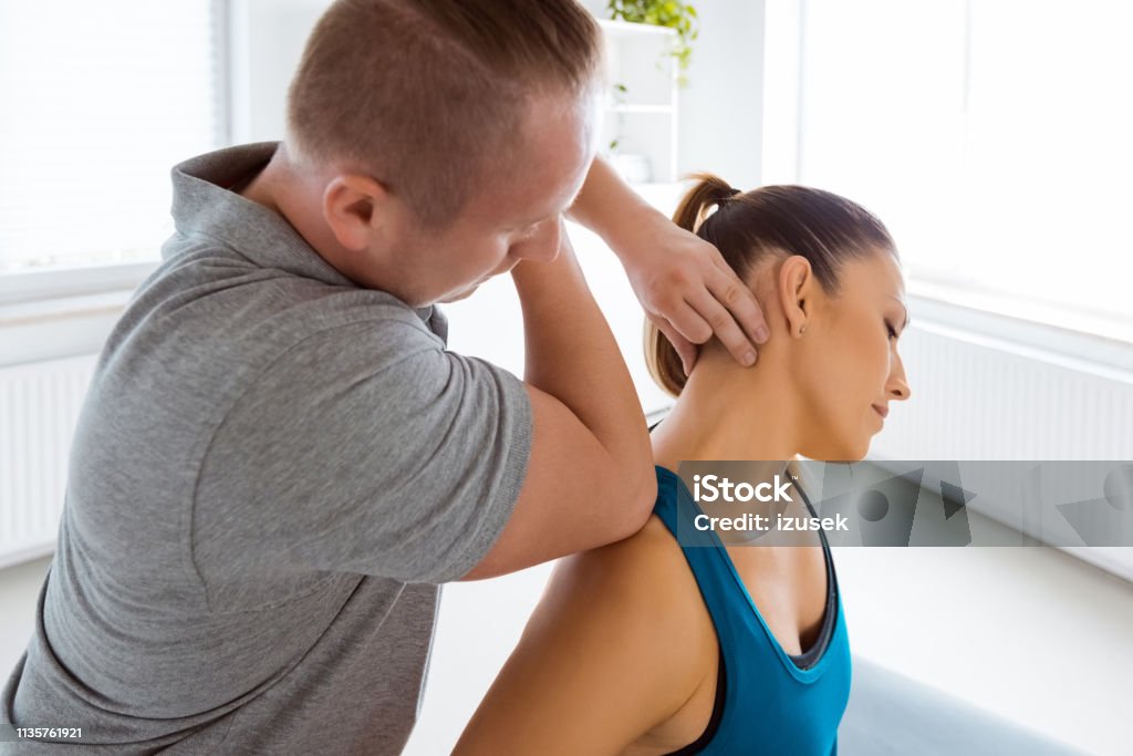 Physiotherapist massaging young woman Manual therapist giving neck massage to young woman in his office. Patient sitting on massage table. Neck Stock Photo