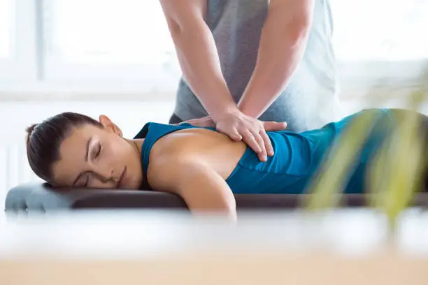 Massage therapist giving back massage to young woman. Patient lying on massage table.